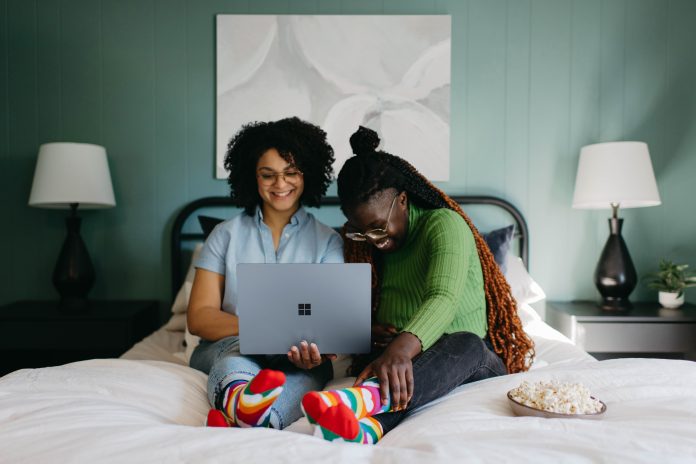 Two women sitting on bed looking at laptop screen